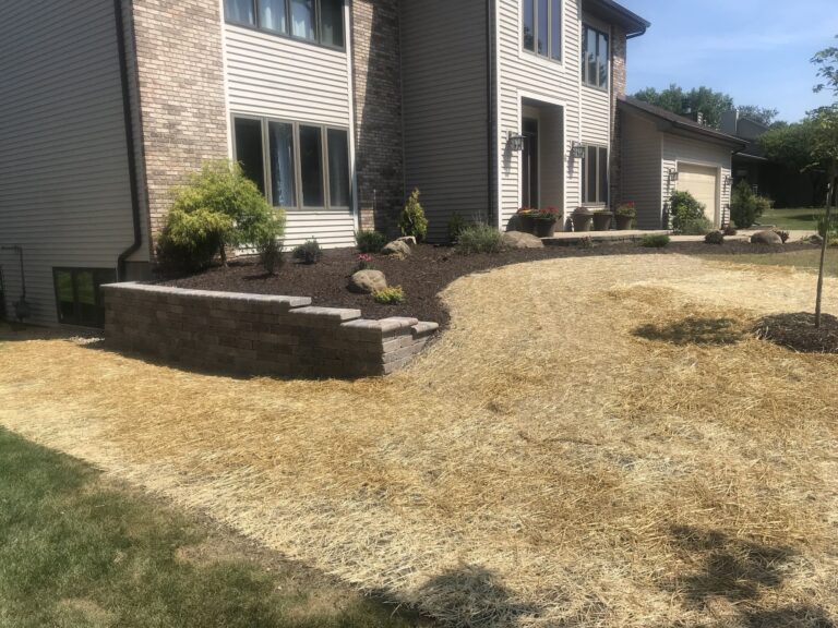 Landscaped yard with retaining wall and straw-covered soil.